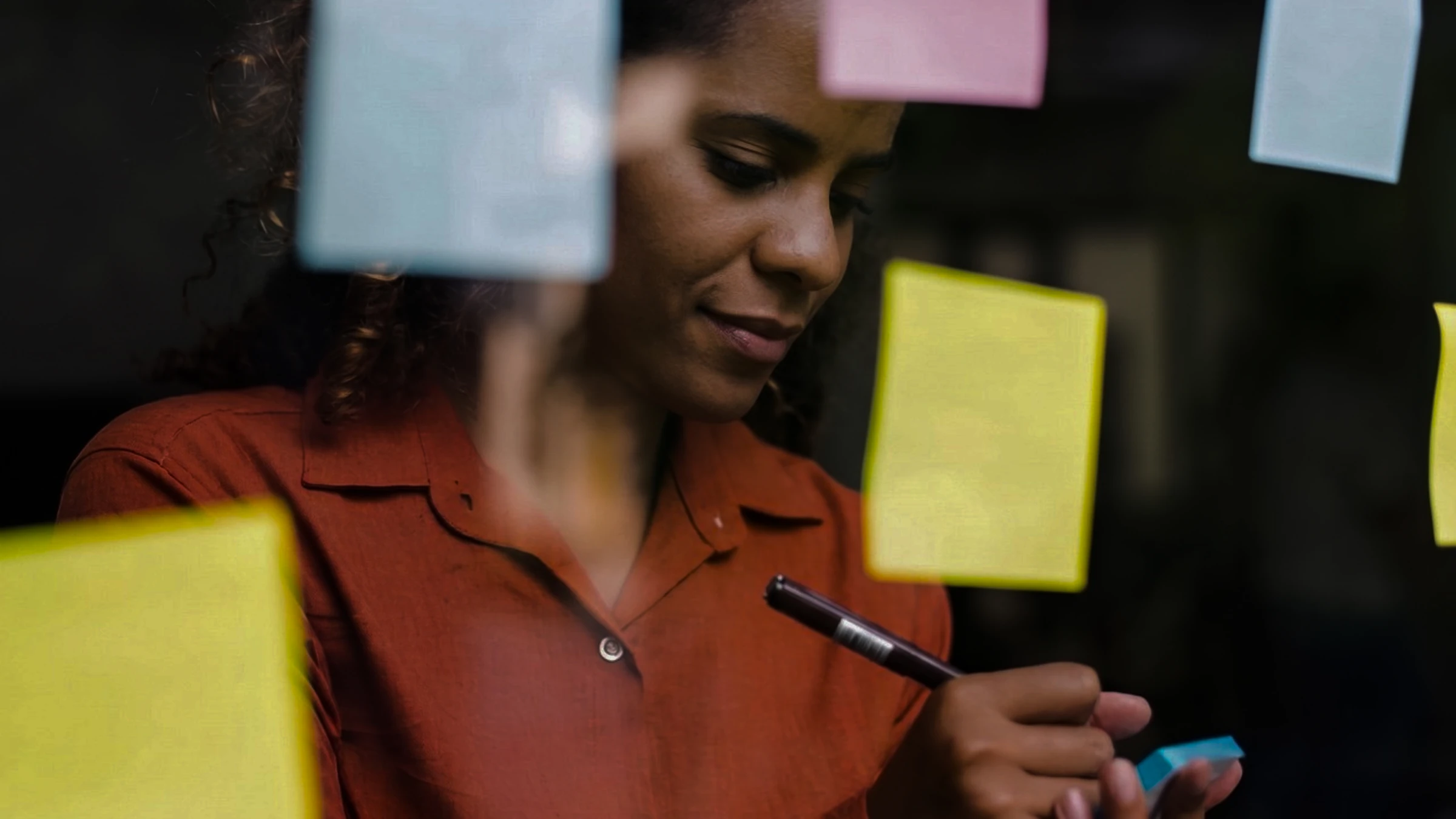 A researcher smiling as she writes on a sticky note, more notes on the glass in front of her.